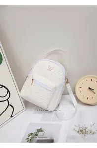 Detail of white quilted mini backpack with a gold butterfly buckle and V-shaped stitching