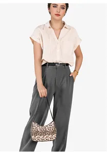 Détail d'un sac demi-lune léopard tenu par un mannequin en chemise rose et pantalon gris