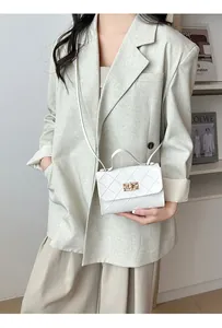 Gedetailleerd zicht op witte gewatteerde tas met gouden draaislot op beige blazer