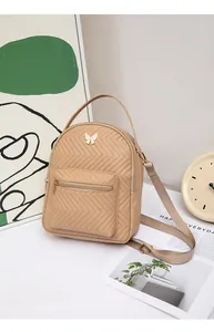 Close-up of khaki quilted mini backpack with pearl butterfly charm and gold hardware