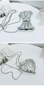 Dettaglio di pochette argentate a forma di cuore e fiocco con eleganti catene a serpente