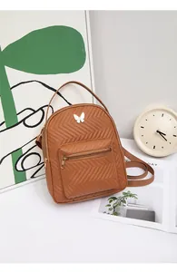 Detail of a brown chevron quilted backpack with a white butterfly ornament and gold zippers
