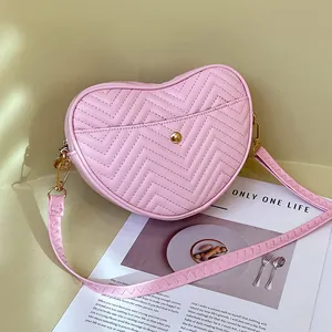 Pink heart-shaped crossbody bag with V-shaped quilting and gold hardware on a magazine