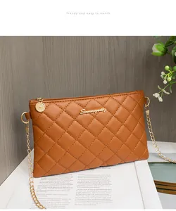 Détail de sac enveloppe matelassé marron avec logo doré, bandoulière chaîne et zip