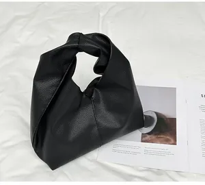 Detail shot of the black lychee pattern leather texture and knot handle on a cloud bag