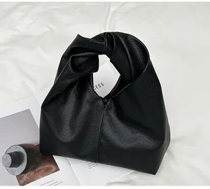 Close-up of black lychee grain leather handbag featuring unique twisted knot handle detail
