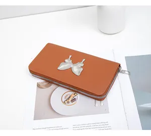 Detail of a brown long zipper wallet with a metallic butterfly charm on a magazine