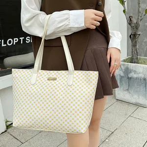 Detail shot of a large beige patterned tote bag featuring golden metal logo and dual handles