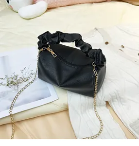 Close-up of black litchi texture crossbody bag with gold chain and pleated handle