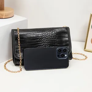 Schwarze Mini-Umhängetasche mit Krokodilprägung, Goldkette und Smartphone zum Größenvergleich
