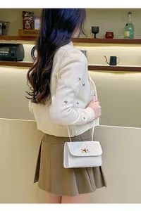 Detailed view of white quilted crossbody bag with gold twist lock on knit cardigan