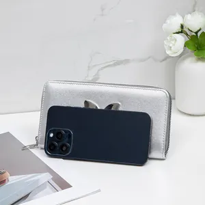 Silver long wallet with metallic finish and bow decor next to a phone for size comparison