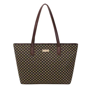 Close-up of geometric monogram pattern and gold logo plaque on a brown tote bag
