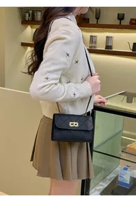 Detail of black quilted crossbody bag with golden twist lock shown on a model