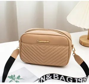 Detail of light brown quilted camera bag with dual zippers and wide canvas shoulder strap