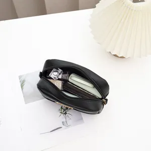 Modern black crossbody bag with V-shaped embroidery and gold hardware on white desk
