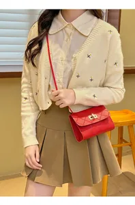 Detail of red quilted crossbody bag with golden twist lock on a beige cardigan outfit