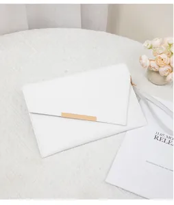 Detail einer weißen Umschlag-Clutch mit Goldplatte auf minimalistischem Hintergrund
