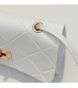 Macro detail of white quilted crossbody bag with gold hardware and lychee grain texture