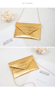 Detail view of gold crocodile embossed envelope crossbody bag with metal chain strap