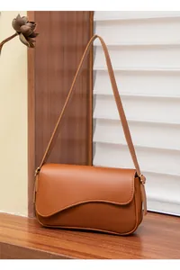 Dettaglio della borsa a tracolla in pelle marrone con design asimmetrico a onde sulla patta