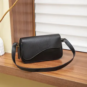 Borsa a tracolla nera con patta ondulata su un espositore in legno minimalista