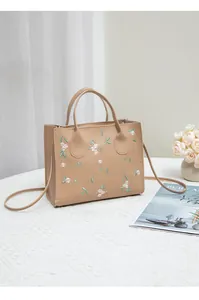 Close-up of pink flower embroidery and green leaves on a beige faux leather handbag