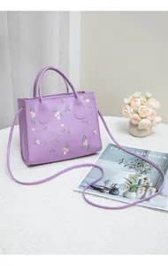 Detail of floral embroidery on a purple faux leather handbag with adjustable strap
