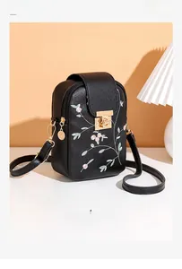 Close-up of floral embroidery on black leather crossbody bag with golden metal clasp