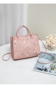 Close-up of elegant floral embroidery on a pink leather handbag with top handles