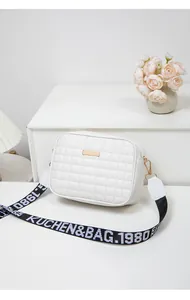 Detail of white quilted crossbody bag with golden metal plate and woven wide strap