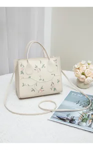 Detailed close-up of pink flower embroidery on a cream white crossbody handbag