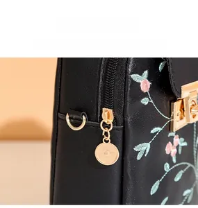 Close-up of floral embroidery and gold metal hardware on a black leather crossbody bag
