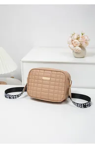 Detail view of beige quilted crossbody bag with golden plate and wide woven shoulder strap