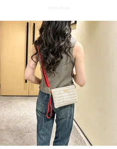Détail du sac bandoulière tissé beige avec sangle rouge et finitions dorées