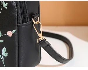 Detail of embroidered floral patterns on black leather bag with gold metal hardware