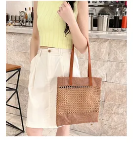Detail of woven straw tote bag featuring leather handles and hollow mesh pattern