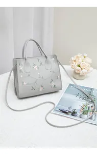 Detail of floral embroidery on a grey crossbody bag with sturdy handles and textured strap