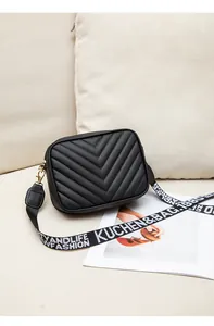 Detail of black V-quilted camera bag with wide patterned strap and golden hardware