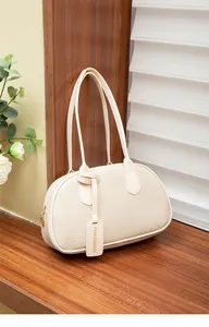 Detail der cremefarbenen Ledertasche mit Kieselstruktur und modischem Logo-Anhänger