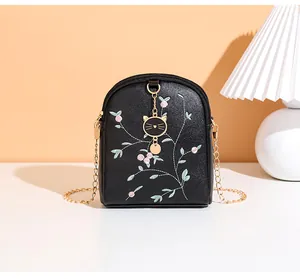 Detailed embroidery of pink flowers and golden cat charm on black crossbody phone bag