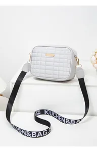 Close-up of grey quilted crossbody bag with gold metal plate and wide lettered strap
