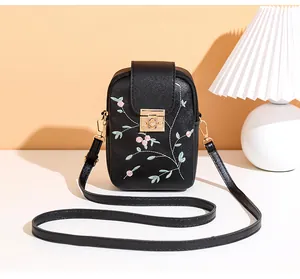 Detail of pink floral embroidery and gold metal clasp on black PU crossbody phone bag