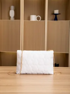 Detail of white heart-quilted crossbody bag with a golden metal chain strap and lock