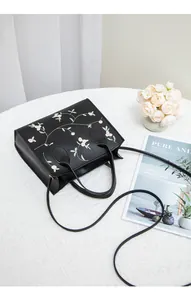 Close-up of black crossbody bag with floral embroidery and detachable strap on white linen