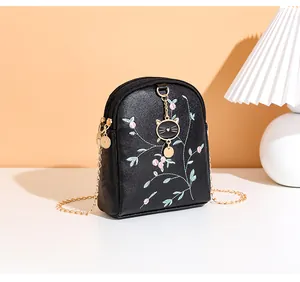 Close-up of floral embroidery and cat pendant on black crossbody phone bag with chain