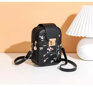 Detail of pink floral embroidery and golden metal twist lock on black leather phone bag