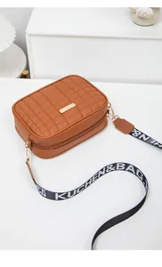 Detail of brown quilted crossbody bag with gold metal trim and branded web shoulder strap