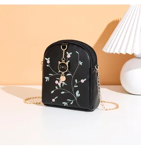 Detail of floral embroidery and cute cat pendant on black crossbody mini chain bag