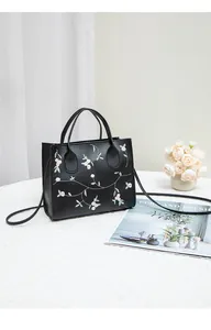 Close-up of pink and white floral embroidery on a black faux leather mini tote bag